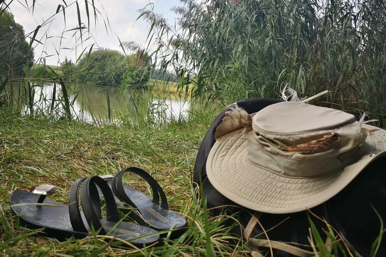 Sonnenhut mit Federn und Sandalen im Gras am Ufer, bereit fuer ein Coaching in der Natur