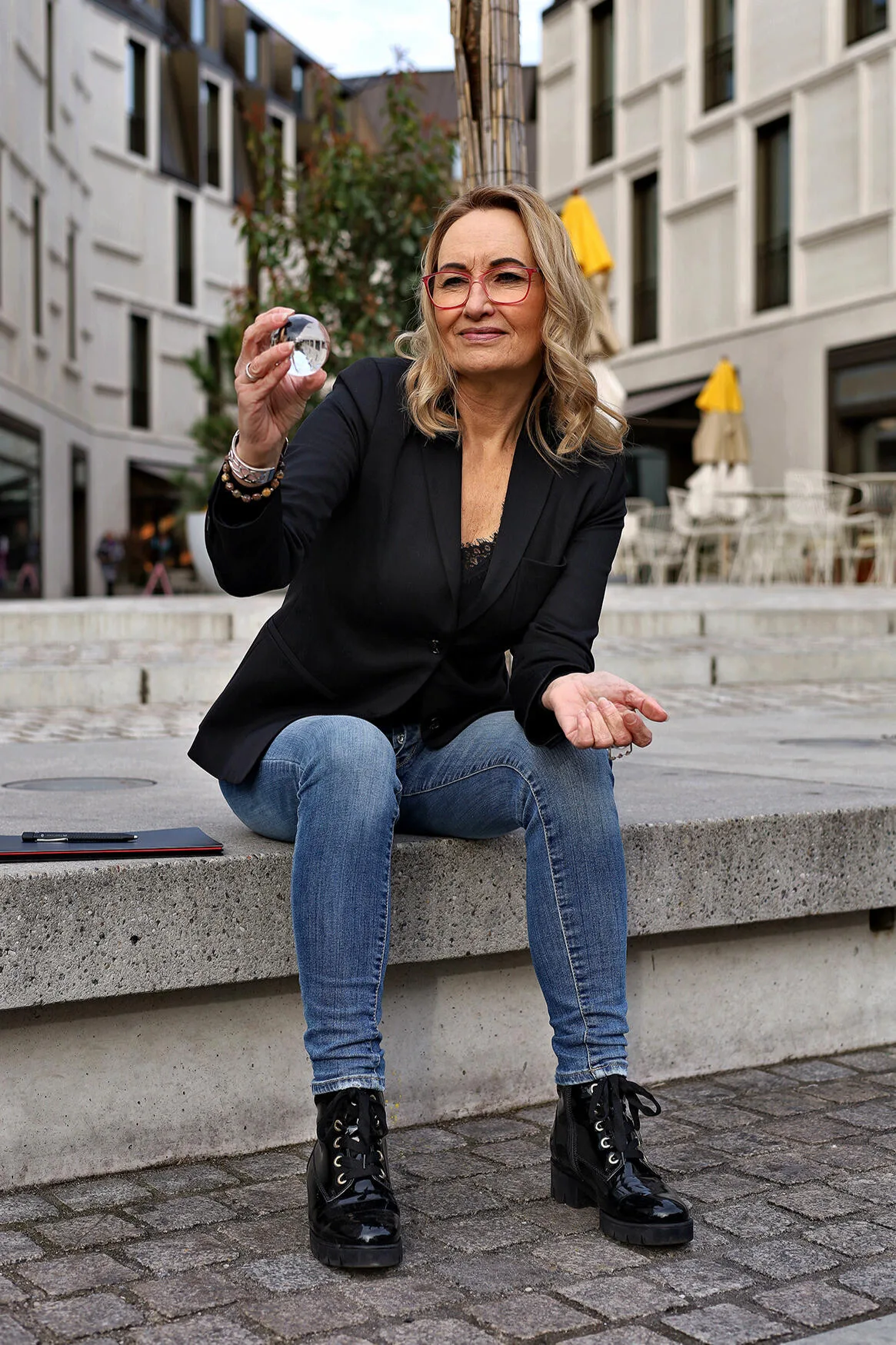 Sabine Rößler sitzt draußen und hält eine kleine Glaskugel in der Hand