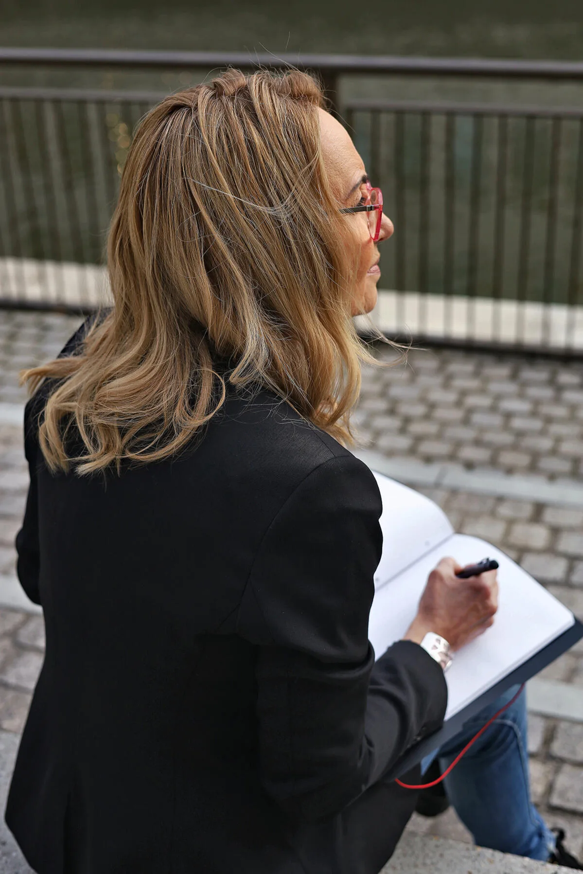 Sabine Rößler sitzt draußen am Wasser und schreibt in ein Notizbuch